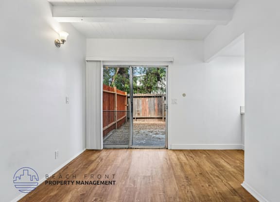 A room with a wooden floor and a sliding glass door leading to a backyard.