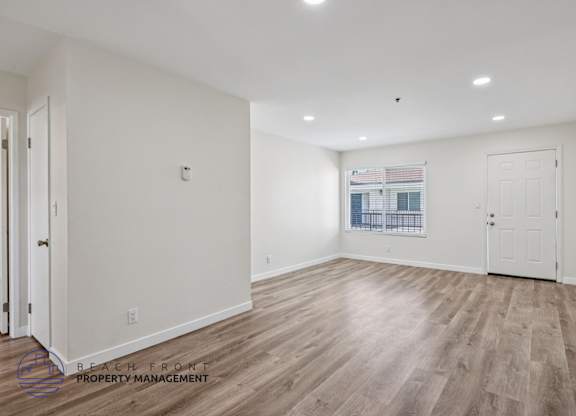 A spacious room with wooden flooring and white walls, with a window showing a view of a balcony.