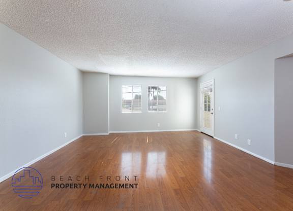 A room with wooden floors and white walls, with a window and a door visible.