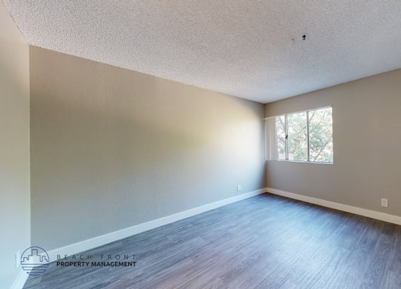 A spacious room with wooden flooring and a window letting in natural light.