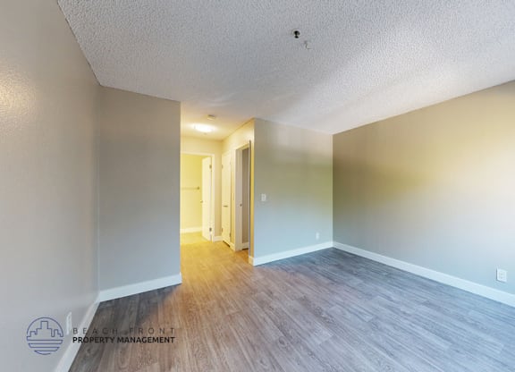 A room with a wooden floor and white walls, with a doorway leading to another room.
