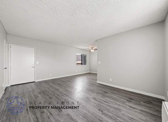 A spacious room with wooden flooring and a logo for Beach Front Property Management in the corner.