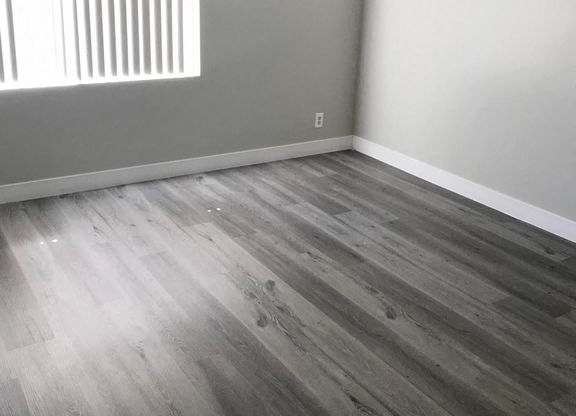 A room with a wooden floor and a window with blinds.