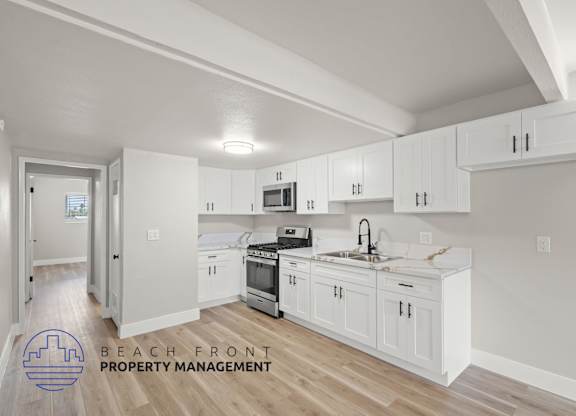 A kitchen with white cabinets and a logo for Beach Front Property Management.