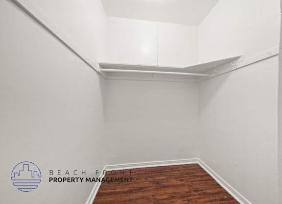 A room with a wooden floor and white walls, with a logo for Beach Front Property Management in the bottom left corner.