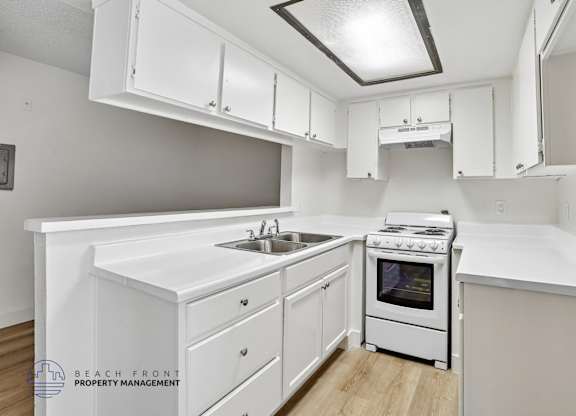A white kitchen with a stove, sink, and cabinets.