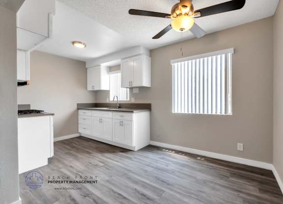 A kitchen with a ceiling fan and wooden flooring.