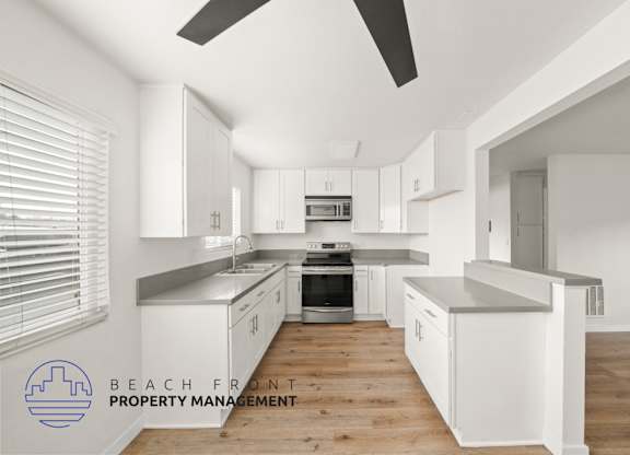 A modern kitchen with white cabinets and a wooden floor.