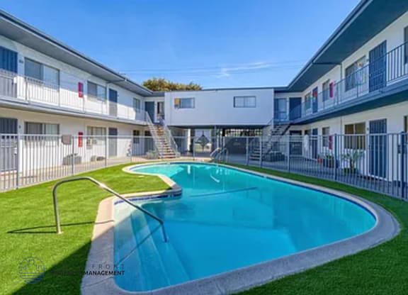 A swimming pool in front of a white building with a metal fence around it.