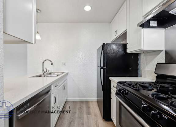 A kitchen with a black fridge and stove top oven.
