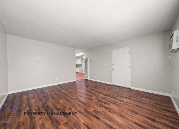 A room with wooden flooring and a logo for Beachfront Property Management on the floor.