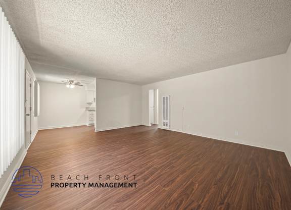 A spacious room with wooden floors and white walls, with a logo for Beach Front Property Management in the bottom left corner.