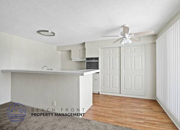 A room with a ceiling fan and a kitchenette.