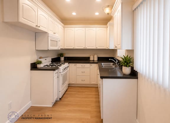 A kitchen with white cabinets and black countertops.