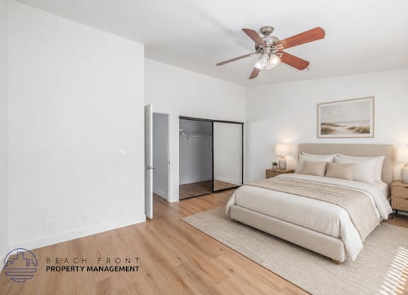 A bedroom with a bed, a ceiling fan, and a nightstand with a lamp.