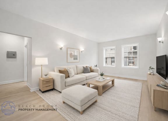 A well-lit living room with a white couch, a white ottoman, and a wooden coffee table.
