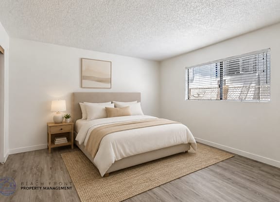 A bedroom with a large bed, a nightstand with a lamp, and a window with blinds.
