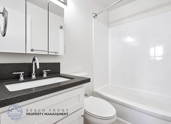 A white bathroom with a black countertop and a shower with a glass door.