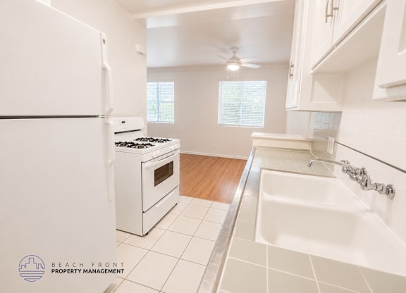A white kitchen with a white fridge, stove, and sink.