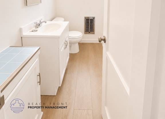 A small white bathroom with a toilet, sink, mirror and a window.
