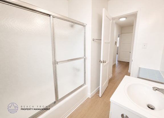 A white bathroom with a sink, mirror, and shower.