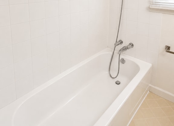 A white bathtub with a shower head and a window with blinds.