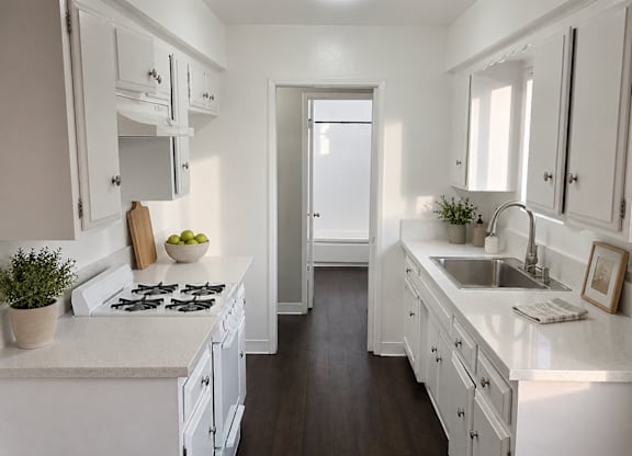 A white kitchen with a stove, sink, and cabinets.