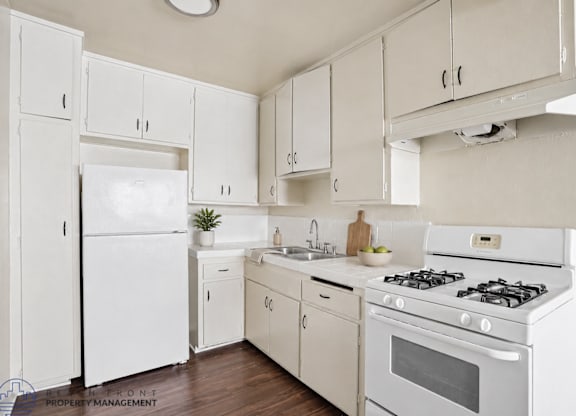 A white kitchen with a refrigerator, oven, and sink.