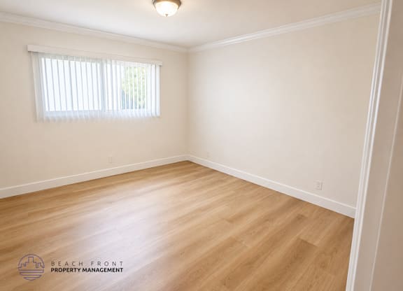 A room with wooden flooring and a window with blinds.