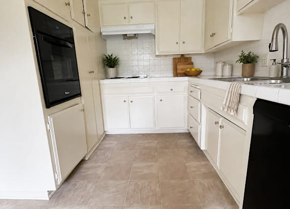 A kitchen with white cabinets and a black fridge.