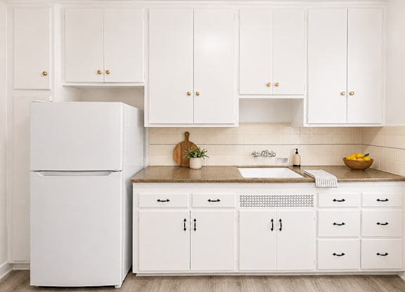A white refrigerator stands next to a kitchen counter with a bowl of fruit on it.