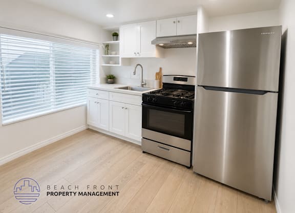A modern kitchen with a stainless steel refrigerator and wooden flooring.