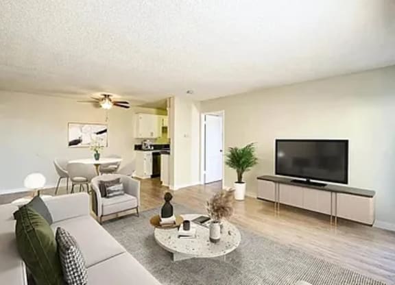 A living room with a grey couch, a white coffee table, a flat screen TV, and a potted plant.