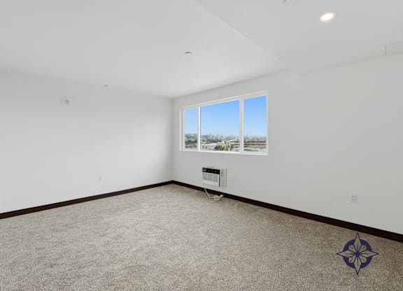 A room with a carpeted floor and a window showing a view of trees and a building outside.