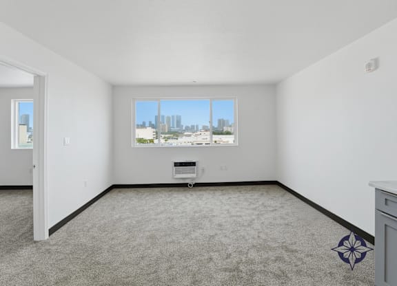 A room with a carpet floor and a window overlooking a cityscape.