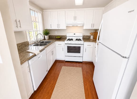 A kitchen with white appliances and wooden floors.