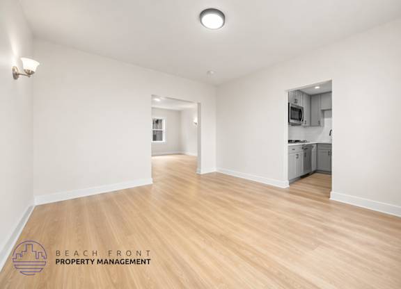 A spacious room with wooden floors and a logo for Beach Front Property Management in the bottom left corner.