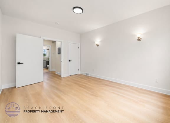 A spacious room with wooden floors and white walls, managed by Beach Front Property Management.