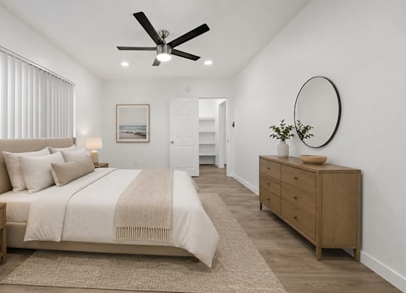 A bedroom with a large bed, a ceiling fan, and a wooden dresser.