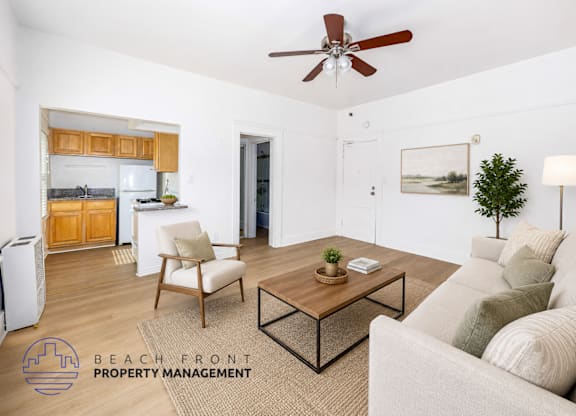 A living room with a couch, chair, and coffee table with a logo for Beach Front Property Management.