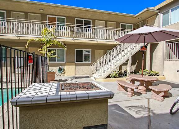 A poolside table with a tiled top is in the foreground of a sunny courtyard.