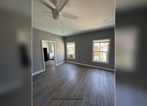 A room with a ceiling fan and two windows.