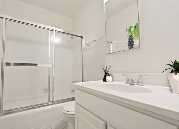 A white bathroom with a glass shower door and a white sink.