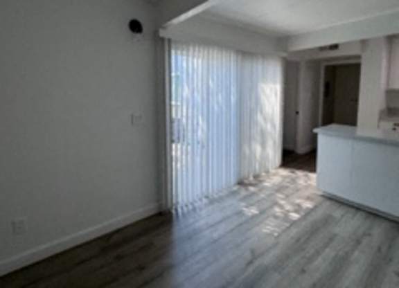 A spacious room with wooden flooring and a window with curtains.