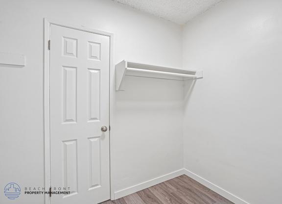 A white door is on the left of a white wall with a shelf on the right.