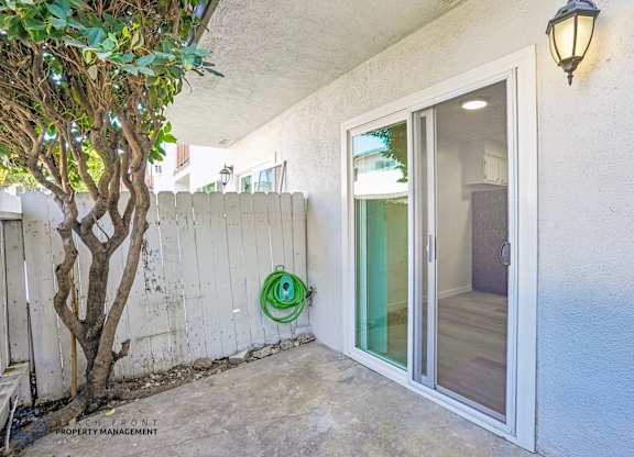 A patio area with a tree, a wall, and a sliding glass door.