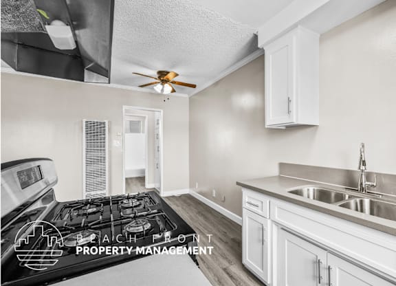 A kitchen with a stove, sink, and cabinets.