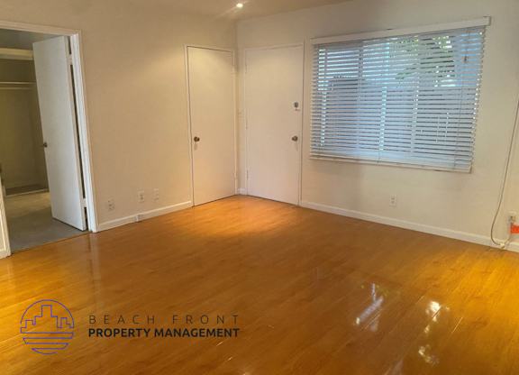 A room with wooden floors and white walls, with a window covered in blinds.