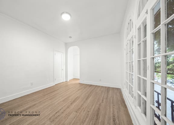 A spacious room with wooden flooring and white walls.