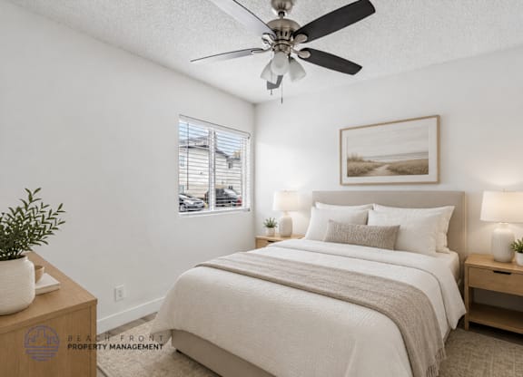 A well-lit bedroom with a large bed, a ceiling fan, and a small table with a plant on it.